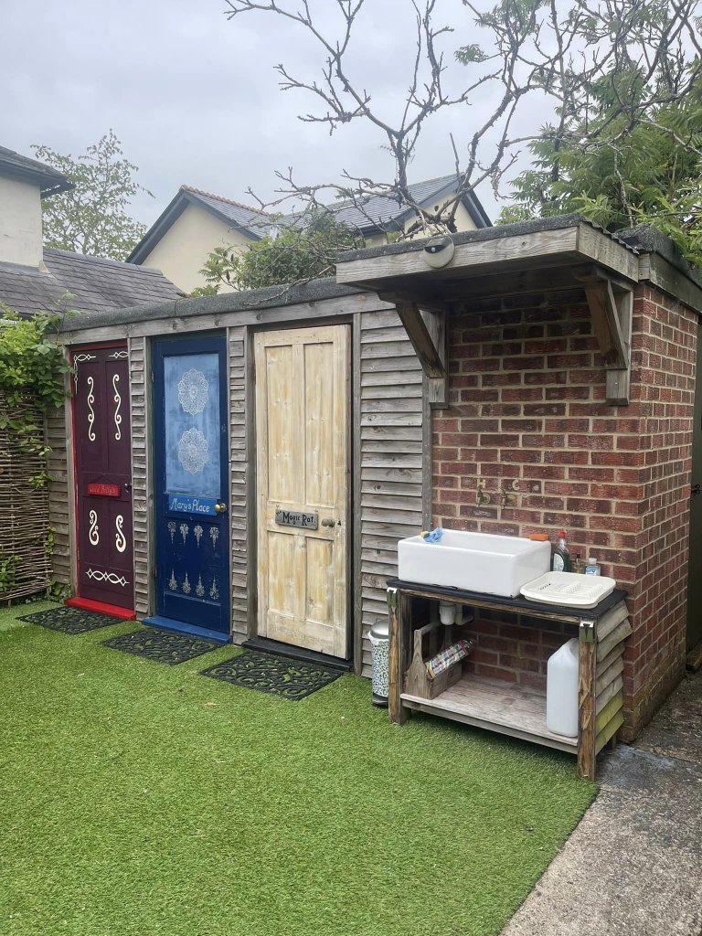 a brick shower block with three colourful doors and an outdoors sink